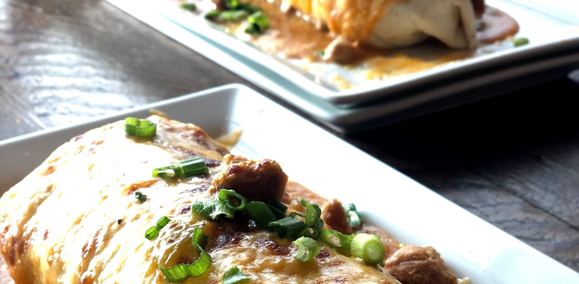 Two breakfast burritos on a plate with cheese and green onions